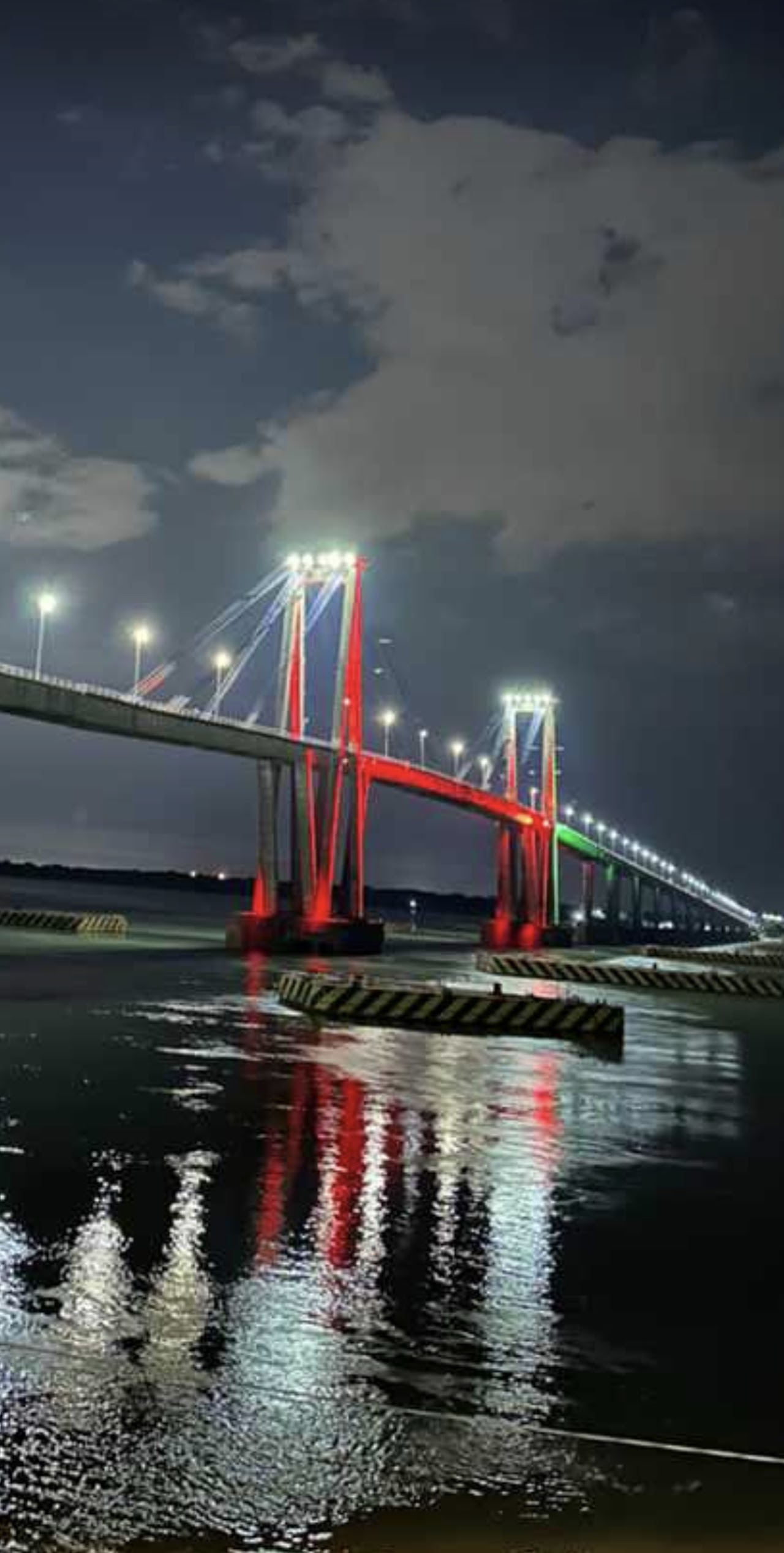 Vista nocturna panorámica de puente con iluminación cálida dorada reflejándose sobre el agua en Resistencia Chaco